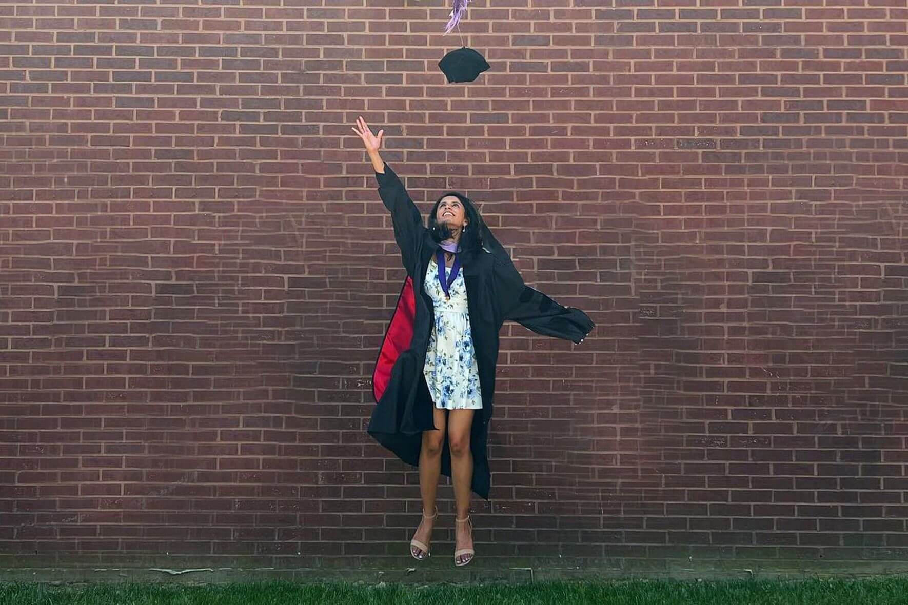 An asian dds girl in a black coat is throwing her graduation cap in the air.